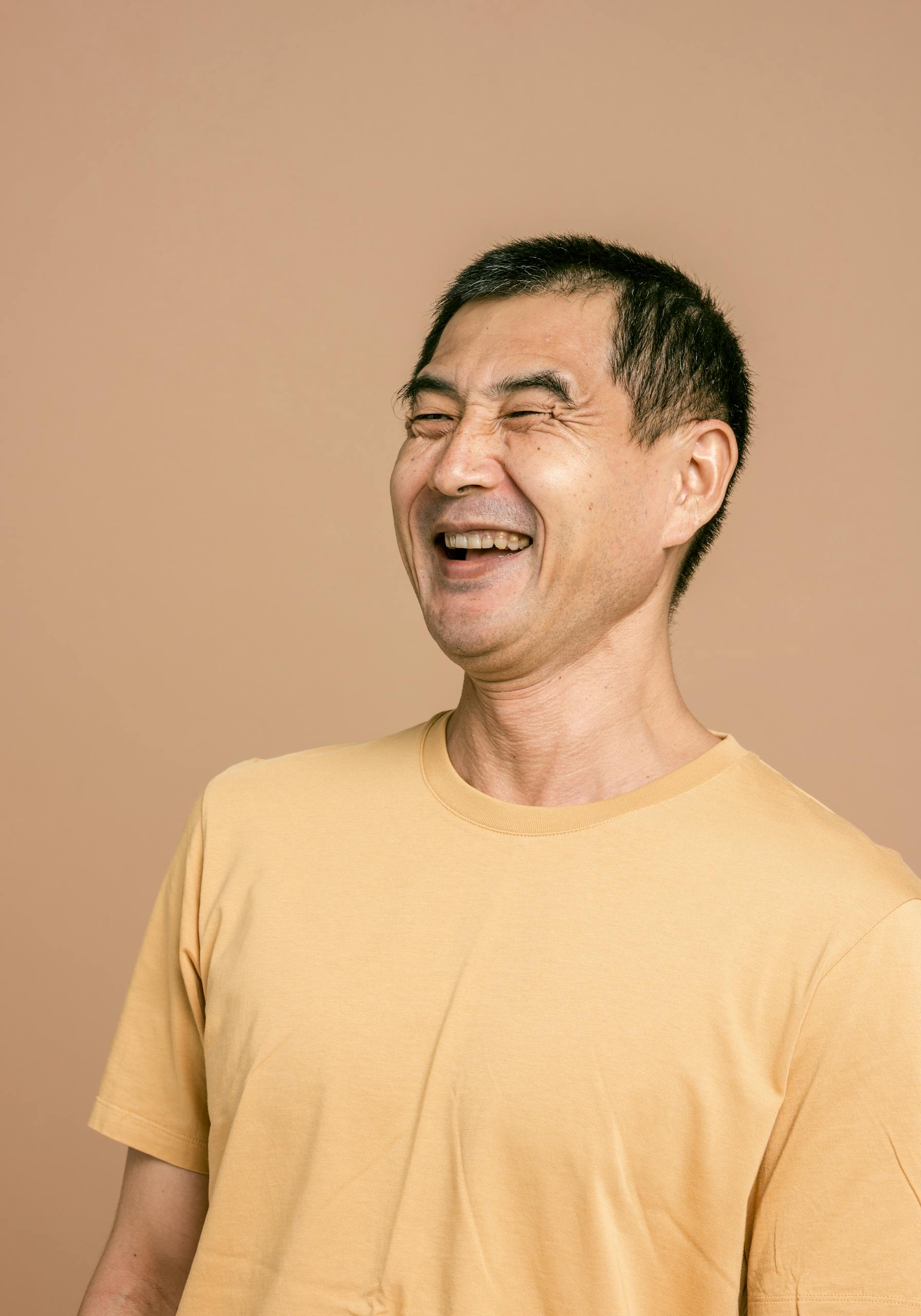 Senior man laughing joyfully in casual t-shirt against a brown background.