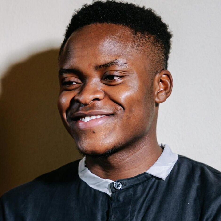 Smiling clergyman in a black robe holding a Bible, engaged in a friendly conversation indoors.